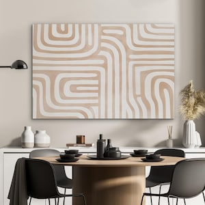 Könnte beinhalten: Abstrakte Kunstleinwand mit beigem Hintergrund und weißen geschwungenen Linien. Das Kunstwerk hängt über einem runden Esstisch aus Holz, der mit schwarzen Tellern, Schalen und Stühlen gedeckt ist. Dekorative Vasen und eine Lampe sind ebenfalls zu sehen.