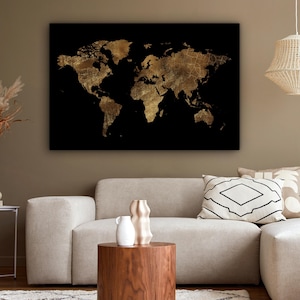 May include: A gold foil world map on a black background. The map is a detailed representation of the continents and countries. The artwork is displayed on a wall in a living room setting, above a beige sofa and a wooden coffee table.
