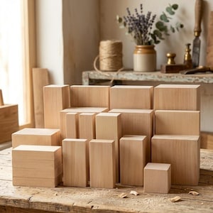 Könnte beinhalten: Eine Ansammlung unbehandelter Holzblöcke in verschiedenen Größen und Formen, die auf einem rustikalen Holztisch angeordnet sind. Die Blöcke sind überwiegend rechteckig und quadratisch, mit natürlicher Holzmaserung. Im Hintergrund ein Fenster, ein Regal mit Dekorationsartikeln und eine Garnrolle.