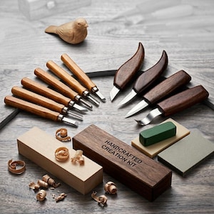 May include: A handcrafted wood carving kit with various tools, including knives and chisels, arranged around a wooden bird figurine. The kit includes a wooden box with the text "Handcrafted Creation Kit".