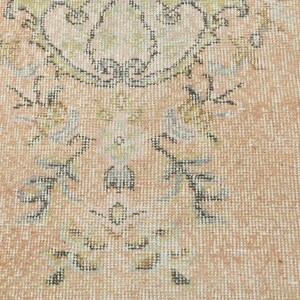 May include: A close-up of a light pink rug with a floral pattern in shades of brown, green, and gray.