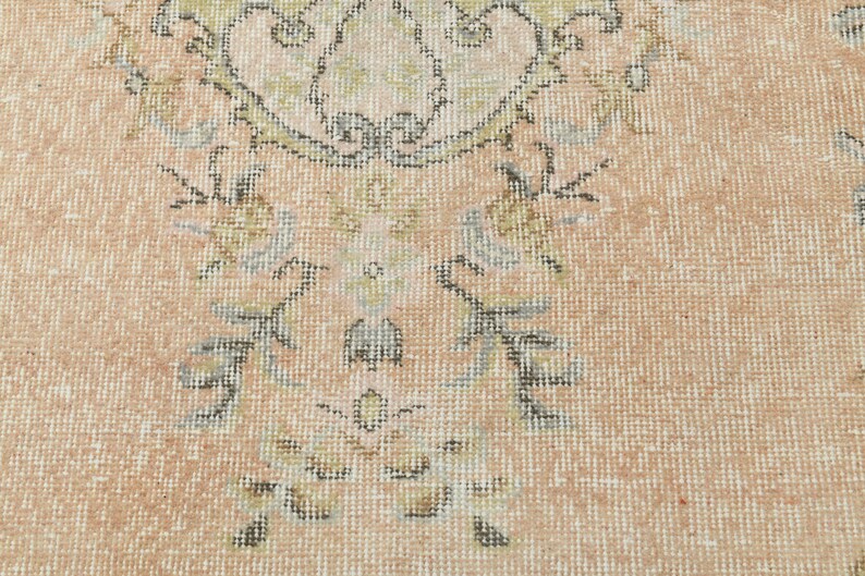 May include: A close-up of a light pink rug with a floral pattern in shades of brown, green, and gray.