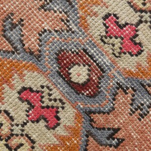 May include: Close-up of a woven rug with a detailed pattern in shades of red, orange, blue, and beige.