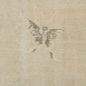 May include: Beige-toned rug with a butterfly design in the center. The butterfly is a dark gray color and appears to be made of small, woven threads. The rug has a textured surface.
