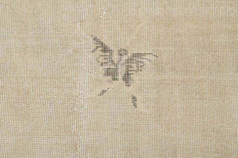 May include: Beige-toned rug with a butterfly design in the center. The butterfly is a dark gray color and appears to be made of small, woven threads. The rug has a textured surface.