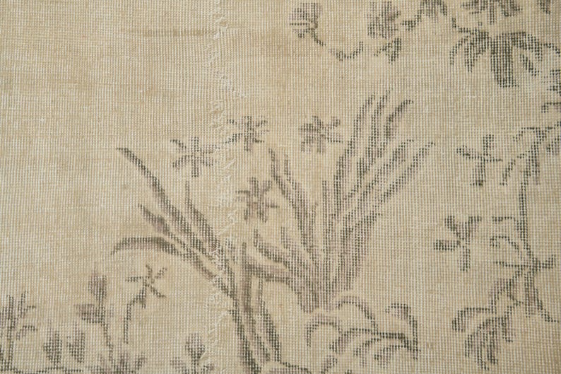 May include: Beige and gray floral patterned rug. The rug features a detailed design of flowers and leaves in shades of gray against a beige background. The rug has a vintage, distressed appearance.