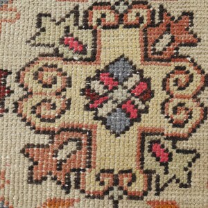 May include: Close-up of a beige rug with a detailed pattern in shades of brown, red, and blue. The pattern features intricate floral motifs and geometric shapes.