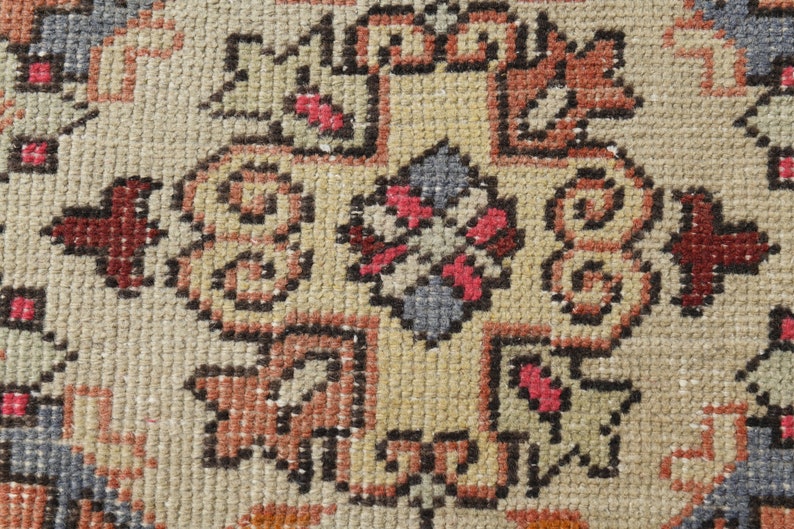 May include: Close-up of a beige rug with a detailed pattern in shades of brown, red, and blue. The pattern features intricate floral motifs and geometric shapes.