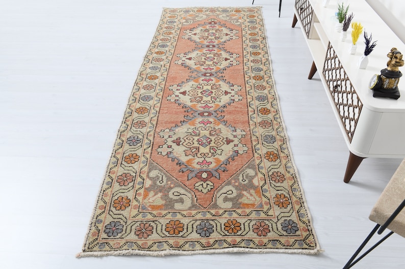 May include: A vintage runner rug with a cream background and a repeating pattern of floral motifs in shades of pink, orange, and blue. The rug has a fringed edge.