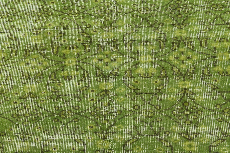 May include: A green vintage rug with a faded floral pattern. The rug has a distressed look and is made of a woven material.