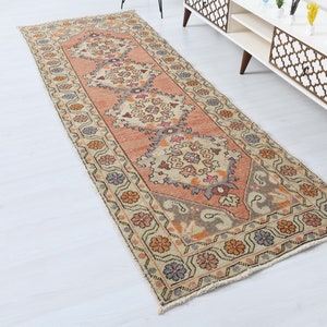 May include: A vintage runner rug with a floral pattern in shades of pink, beige, and brown. The rug has a fringed edge and is made of wool.
