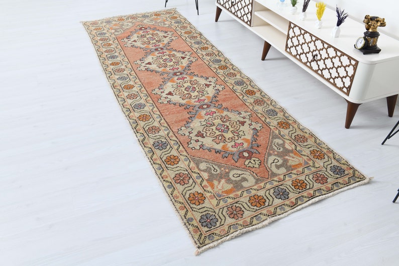 May include: A vintage runner rug with a floral pattern in shades of pink, beige, and brown. The rug has a fringed edge and is made of wool.