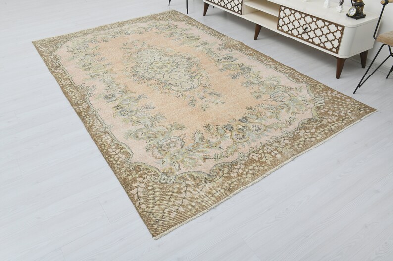 May include: A vintage rug with a light pink background and a brown floral pattern. The rug has a distressed look and is perfect for adding a touch of bohemian style to your home.