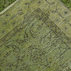 May include: Close-up of a green rug with a woven pattern. The rug has a fringe border.