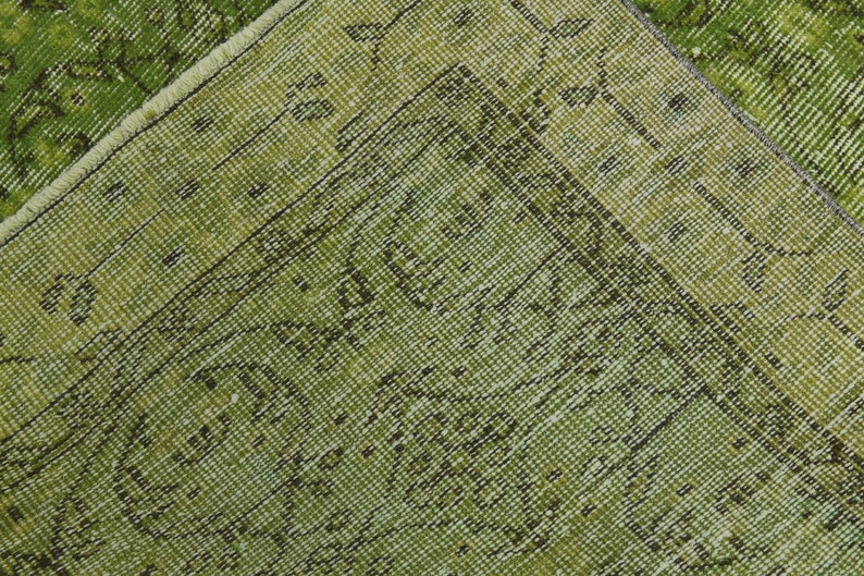 May include: Close-up of a green rug with a woven pattern. The rug has a fringe border.