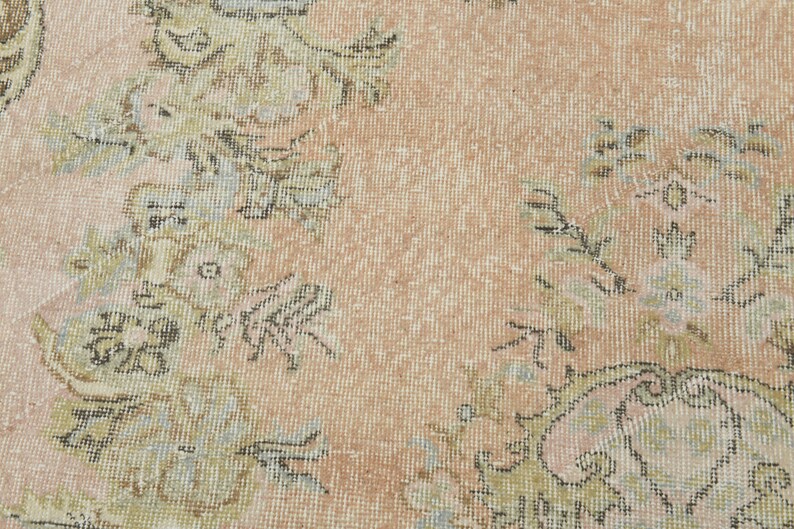 May include: A close-up of a light pink rug with a floral pattern. The rug has a woven texture and features intricate details in shades of beige, brown, and blue.