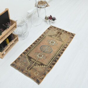 May include: A rectangular area rug featuring a faded tan and brown color palette with intricate geometric patterns, including central medallions and a dark border. The rug displays a worn texture with visible signs of age and detailed motifs.