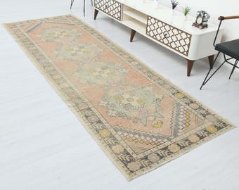 Puede incluir: Una alfombra de pasillo vintage con fondo rosa claro y un patrón floral en tonos beige, gris y rosa. La alfombra tiene un borde geométrico en negro y blanco.