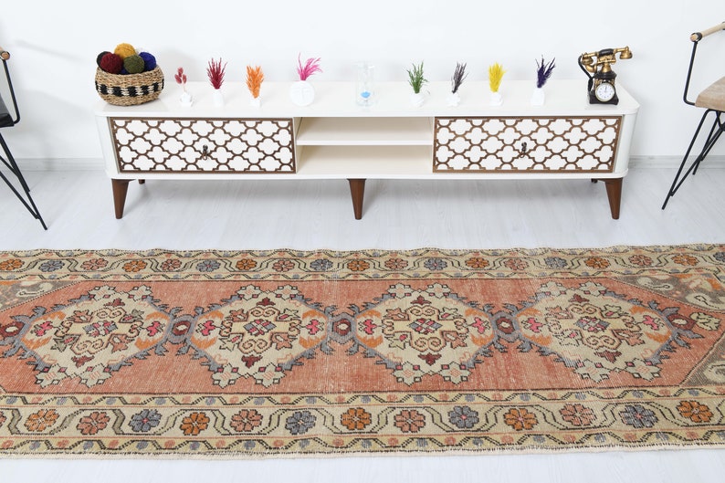 May include: A vintage runner rug with a peach background and intricate floral patterns in shades of beige, brown, and blue. The rug has a distressed look and is perfect for adding a touch of bohemian style to any room.