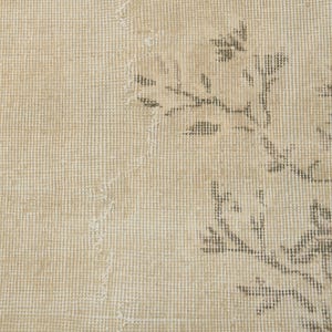 May include: Close-up of a beige rug with a floral pattern in shades of brown and gray. The rug has a textured surface and a distressed appearance, suggesting an antique or vintage style. The design is visible on the right side.