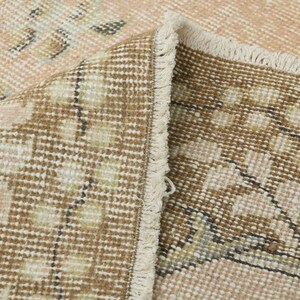May include: Close-up of a brown and cream patterned rug with a fringe border. The rug has a woven texture and a subtle pink hue.