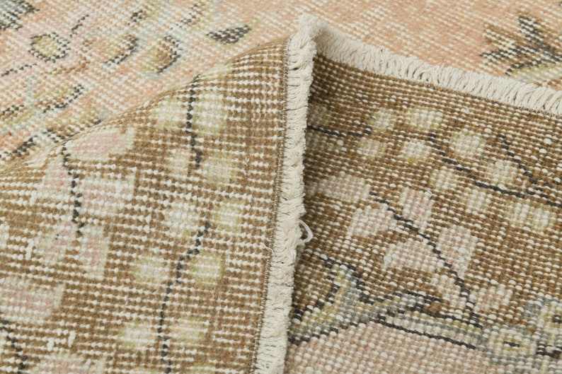 May include: Close-up of a brown and cream patterned rug with a fringe border. The rug has a woven texture and a subtle pink hue.