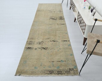 May include: A rectangular beige runner rug with a distressed design. The rug features dark brown and teal accents, with a faded, vintage aesthetic. The rug's dimensions are not visible in the image.