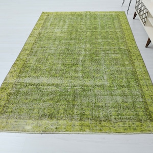 May include: A green vintage rug with a faded floral pattern and a border. The rug has a distressed look and is made of natural fibers.