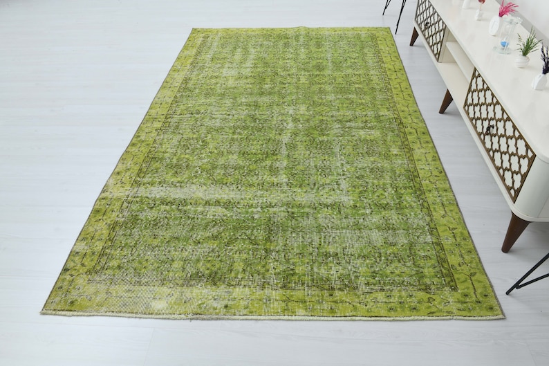 May include: A green vintage rug with a faded floral pattern and a border. The rug has a distressed look and is made of natural fibers.