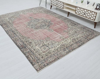 May include: A vintage-style rug with a faded pink center and intricate floral patterns in shades of beige, gray, and black. The rug has a distressed look and a worn, faded appearance.