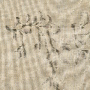 May include: Close-up of a beige rug with a floral pattern in shades of gray. The rug has a textured surface and a faded, vintage appearance. The floral design is spread across the rug.