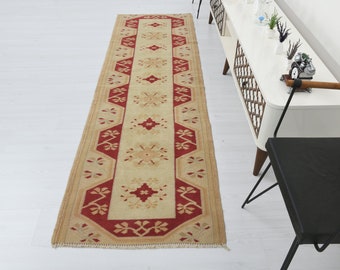 May include: A long, rectangular runner rug with a cream background and a red border. The rug has a traditional floral pattern in the centre and a geometric pattern along the edges.