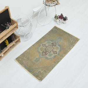 May include: A rectangular area rug featuring a faded mustard yellow background with a central geometric medallion in muted shades of blue, brown, and cream. The rug has a distressed texture and short fringe on the ends, displayed on a white floor.