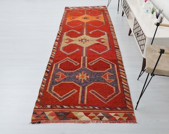 May include: A long, rectangular red, orange, and blue patterned rug with a geometric design. The rug has a fringe border.