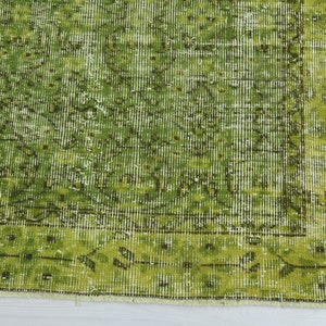 May include: A green vintage rug with a faded floral pattern. The rug has a fringed edge and is made of a soft, woven material.