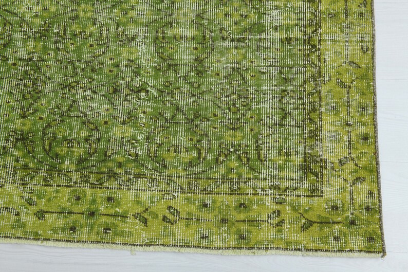 May include: A green vintage rug with a faded floral pattern. The rug has a fringed edge and is made of a soft, woven material.
