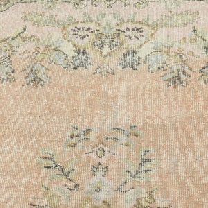 May include: A vintage rug with a floral pattern in shades of pink, beige, and brown. The rug has a distressed look and is woven with a fine texture.
