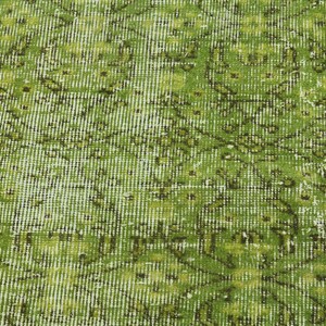 May include: A close-up of a green and white patterned rug with a distressed look. The rug has a woven texture and a faded appearance.