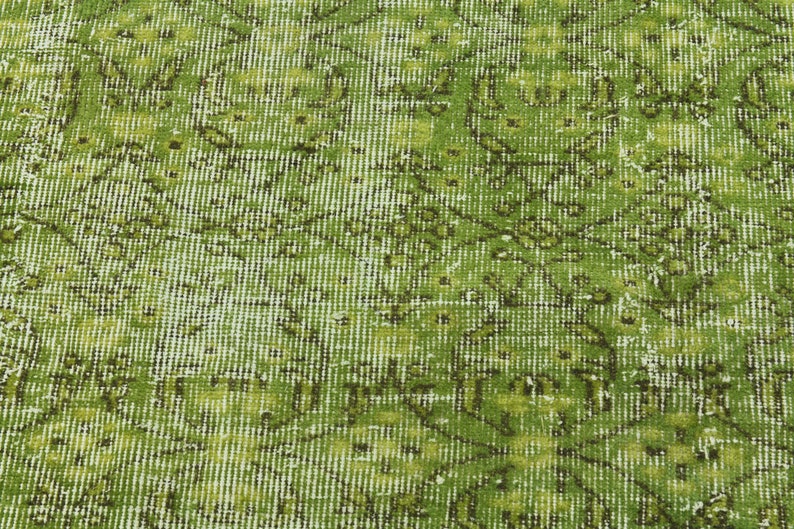 May include: A close-up of a green and white patterned rug with a distressed look. The rug has a woven texture and a faded appearance.