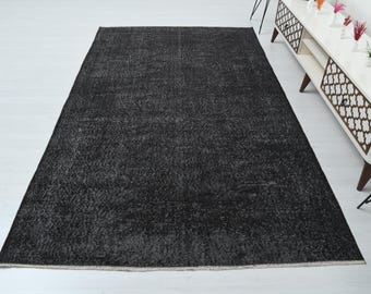 May include: A large, rectangular, dark gray rug with a textured surface. The rug has a lighter border and is placed on a white floor. The rug is a home decor item.