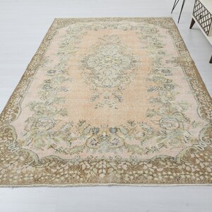 May include: A vintage rug with a light pink background and a floral pattern in shades of brown and green. The rug has a decorative border with a floral design.