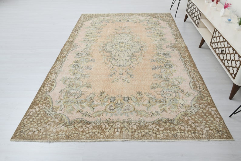 May include: A vintage rug with a light pink background and a floral pattern in shades of brown and green. The rug has a decorative border with a floral design.