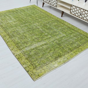 May include: A green vintage rug with a faded floral pattern and a dark green border. The rug has a distressed look and is made of natural fibers.