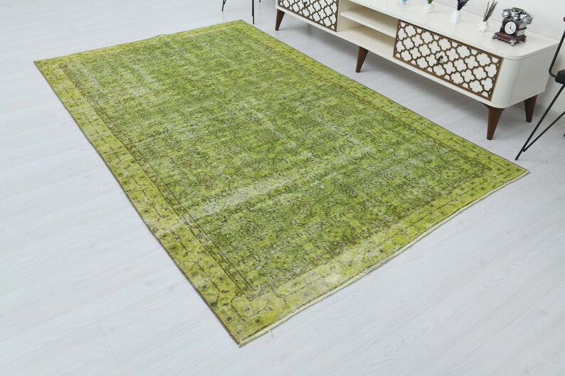May include: A green vintage rug with a faded floral pattern and a dark green border. The rug has a distressed look and is made of natural fibers.