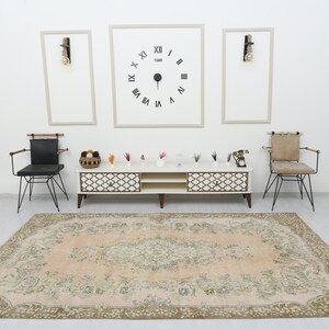 May include: A light pink vintage rug with a floral pattern, two black chairs with wooden arms, a white entertainment center with two shelves and a clock on the wall that reads "TIME" with Roman numerals.