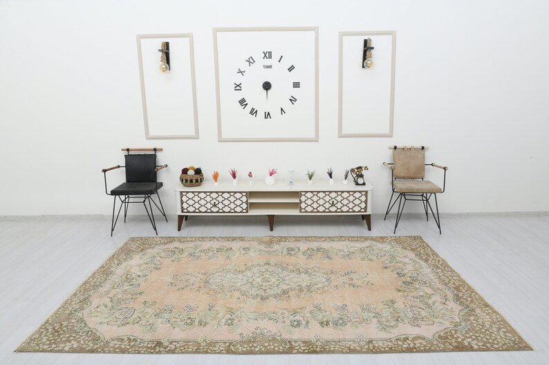 May include: A light pink vintage rug with a floral pattern, two black chairs with wooden arms, a white entertainment center with two shelves and a clock on the wall that reads "TIME" with Roman numerals.