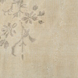 May include: Close-up of a beige rug with a floral pattern in shades of gray. The rug has a distressed, vintage look with visible wear and tear, adding to its character. The design is centered on the left side.