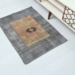 Puede incluir: Una pequeña alfombra vintage gris y rosa con un patrón geométrico. La alfombra tiene un aspecto descolorido y desgastado, perfecto para añadir un toque de estilo bohemio a cualquier habitación.