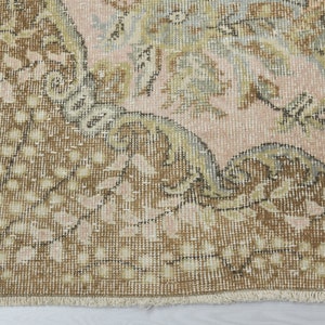 May include: A vintage rug with a floral pattern in shades of brown, pink, and beige. The rug has a fringe border and a worn, distressed look.