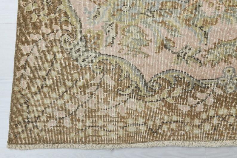 May include: A vintage rug with a floral pattern in shades of brown, pink, and beige. The rug has a fringe border and a worn, distressed look.